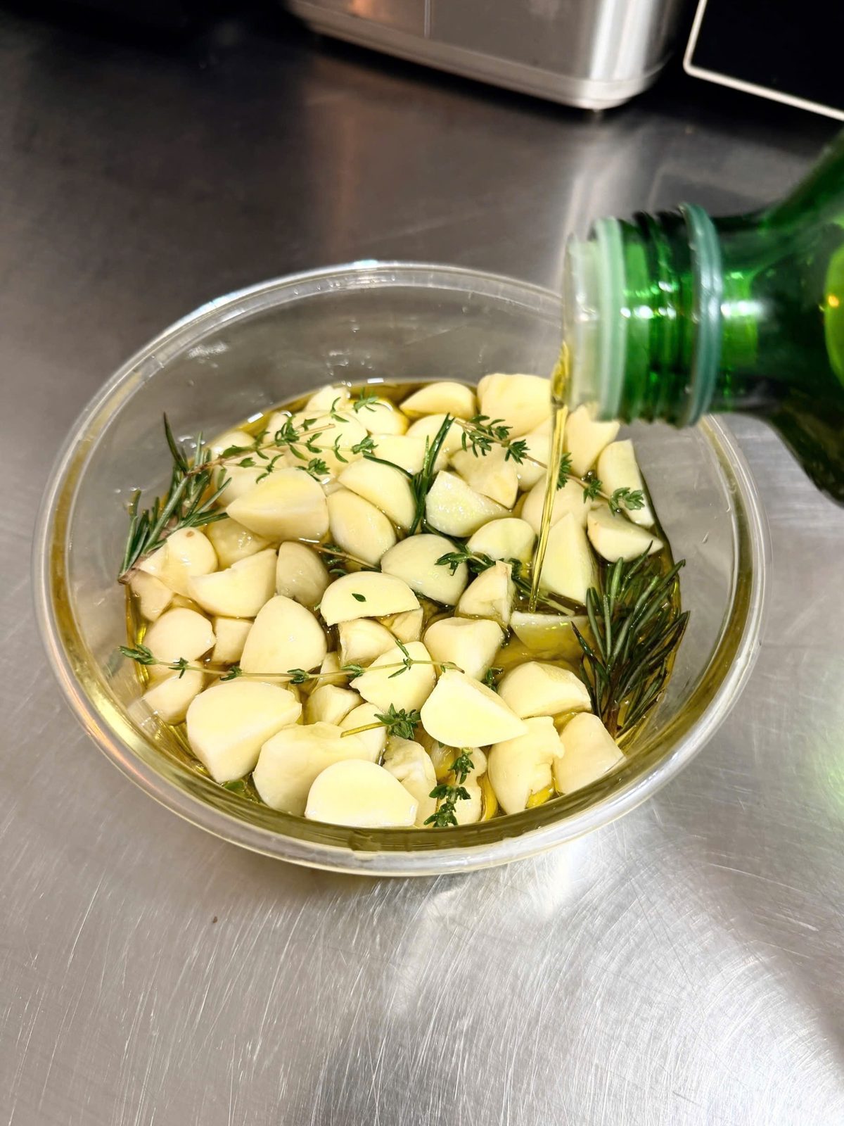 Bếp sơ chế: tỏi và thảo mộc ngâm dầu confit — không phải một ly nước uống